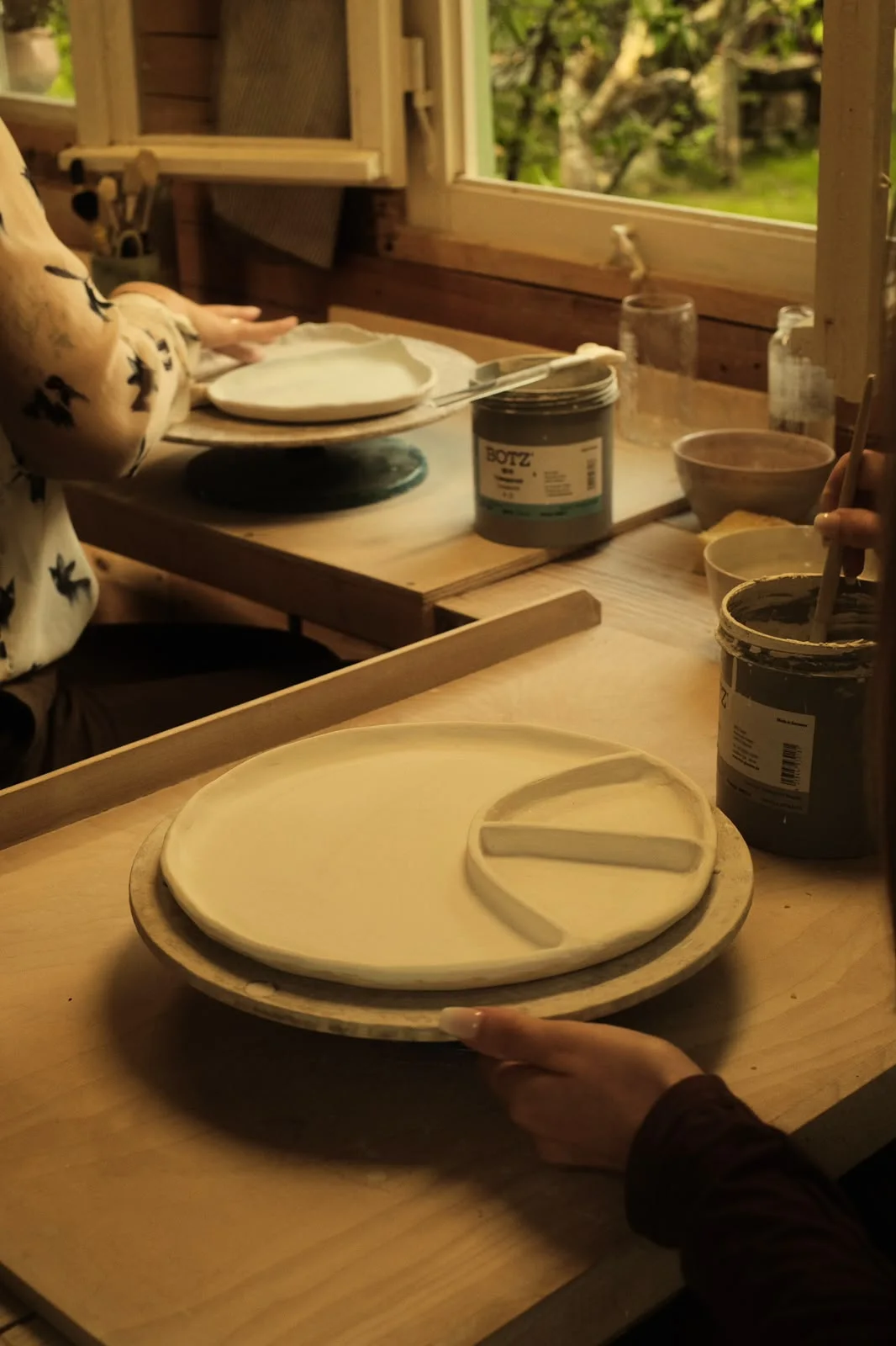 Selbst getöpferte Teller und Glasuren auf dem Arbeitstisch im Atelier